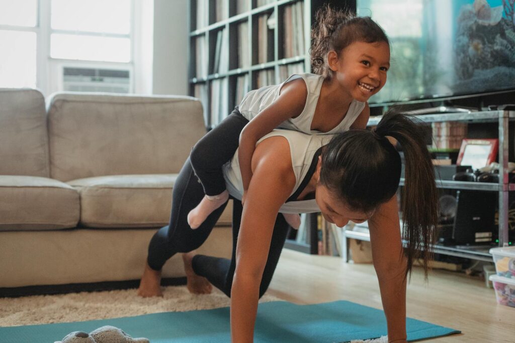 Young Asian woman piggybacking smiling daughter while working on her weak  core at home