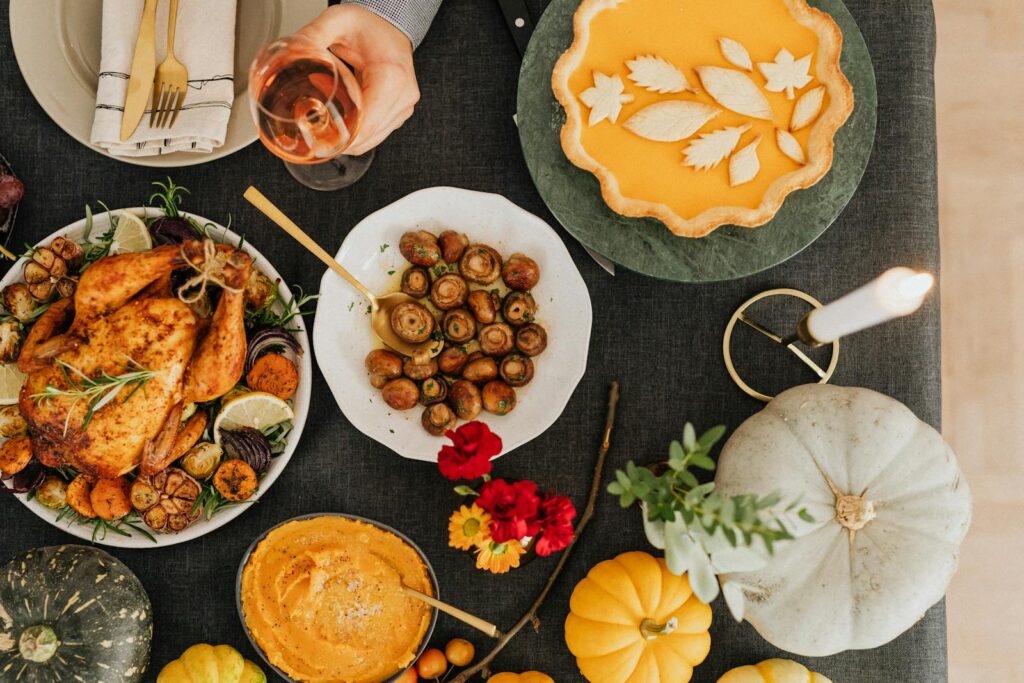 A top-down view of a festive autumn dinner featuring roast chicken, pumpkin pie, and various side dishes.